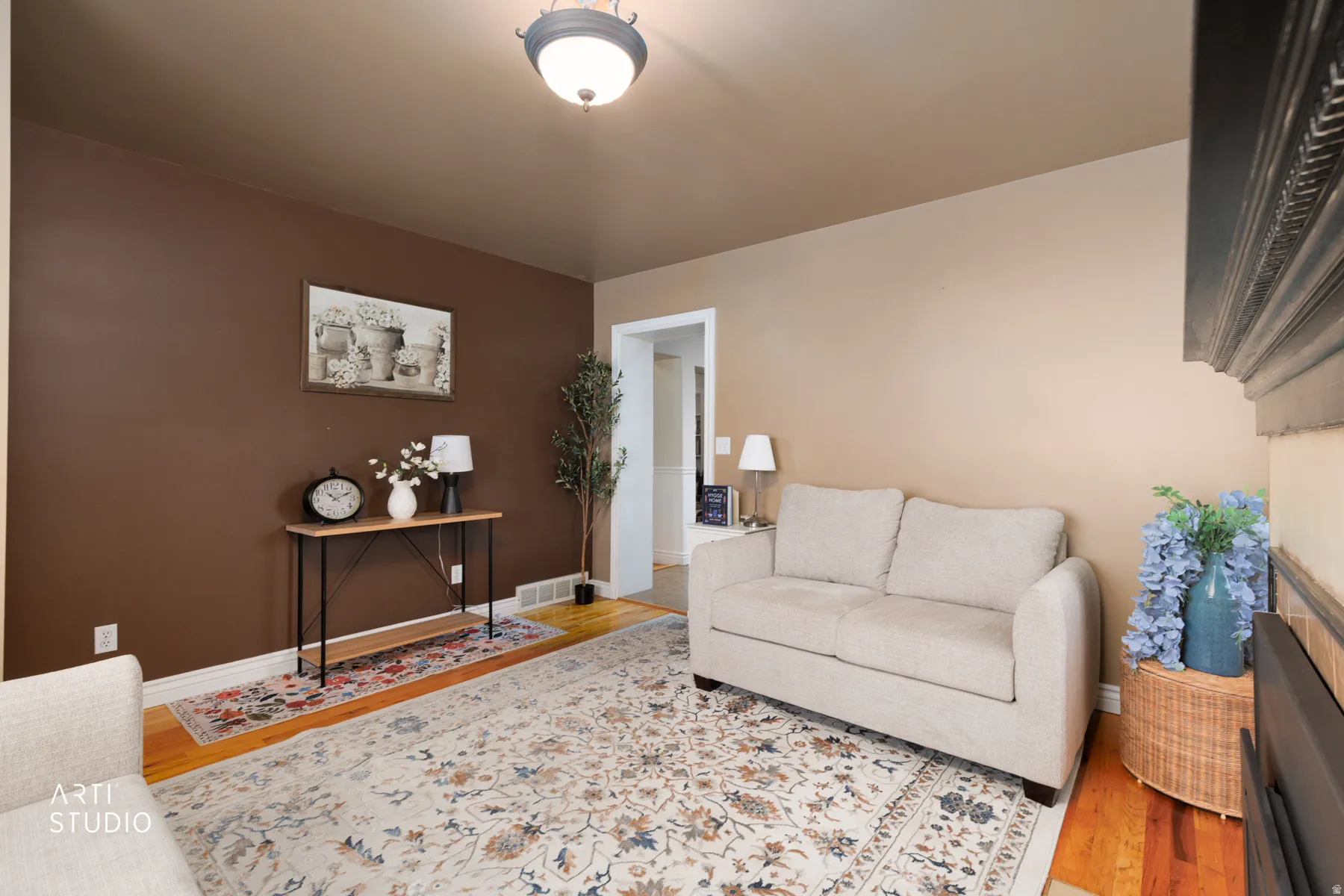 Warm-toned interior room featuring wood-finish flooring, a decorative ceiling light fixture, and a sculpted dark wood mantel