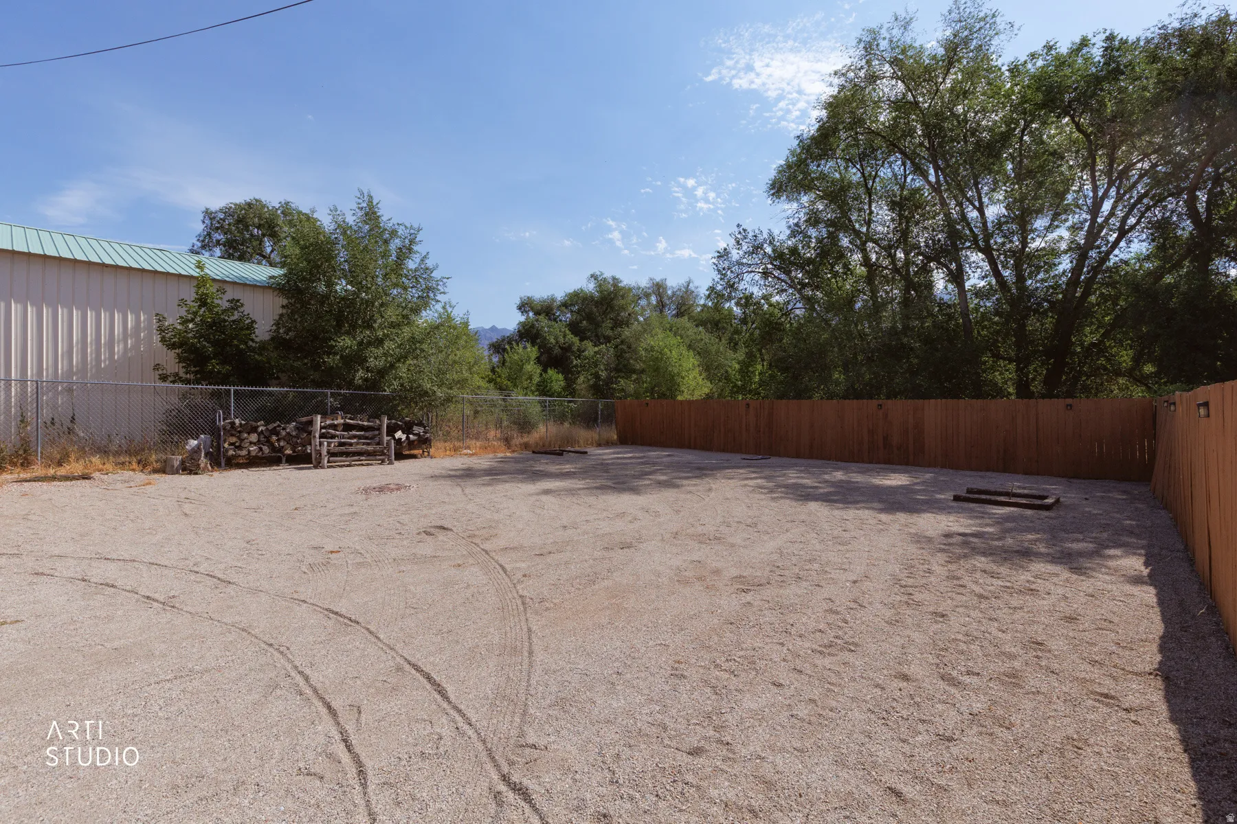 Expansive gravel lot featuring a chain-link fence, wood privacy fence, and mature trees
