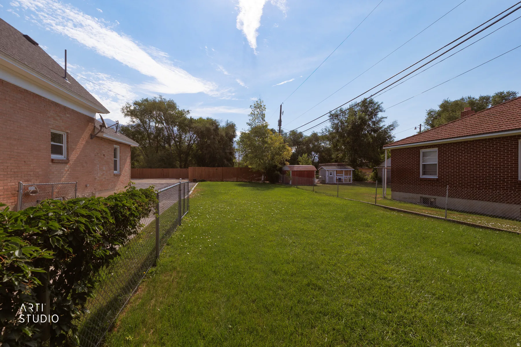 Expansive grass lawn featuring a chain-link fence, mature trees, and two outbuildings