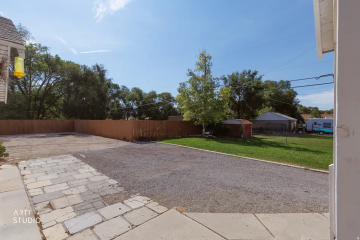 Expansive backyard area featuring a gravel surface, a wooden privacy fence, natural grass sections, and mature trees