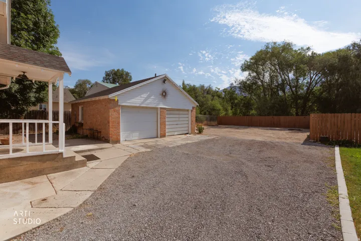 Two-car garage with brick siding, white garage doors, and an expansive gravel driveway