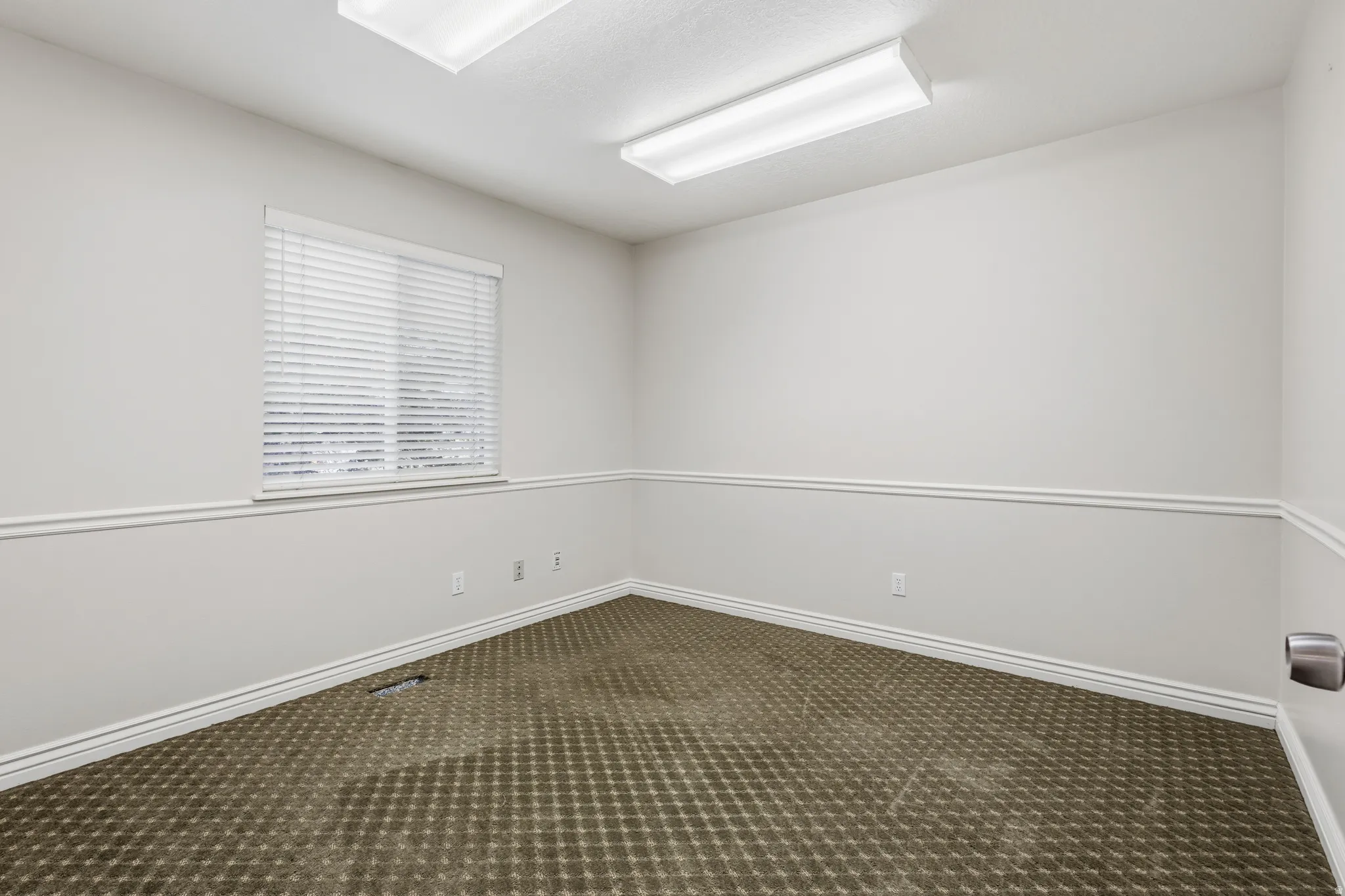 Neutral-toned interior room featuring a window with white blinds, crown molding, and a patterned carpet