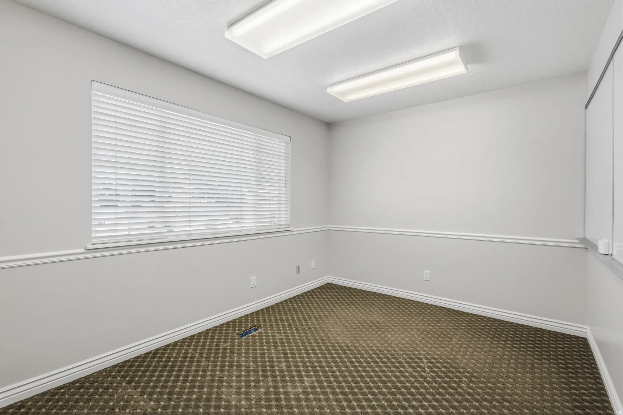 Room featuring a large window with white blinds, neutral wall paint, white crown molding and baseboards, and patterned carpet flooring