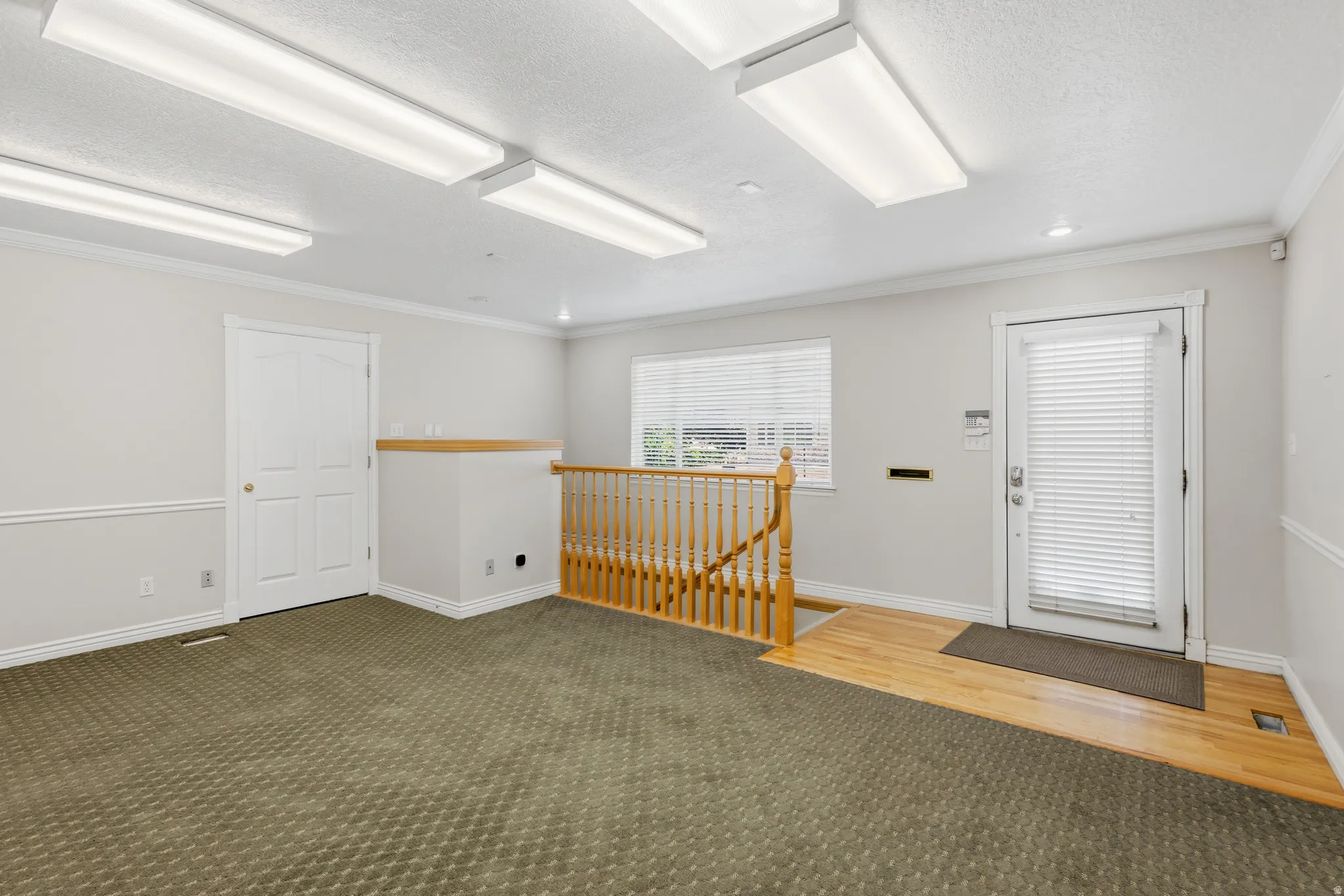 Versatile space featuring recessed lighting, a door with integrated blinds, and a built-in wooden staircase with a matching railing