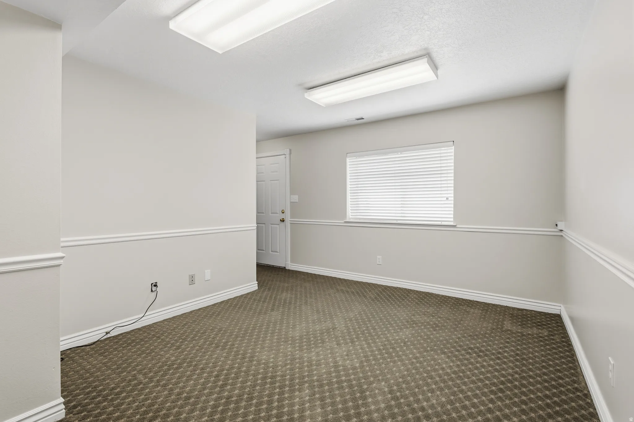 Spacious room featuring neutral paint tones, crown molding, chair rail detailing, patterned carpeting, and recessed lighting fixtures