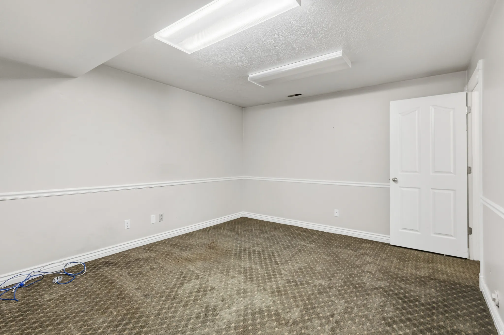 Neutral-toned room featuring a textured carpet, white baseboards, and decorative chair rail molding