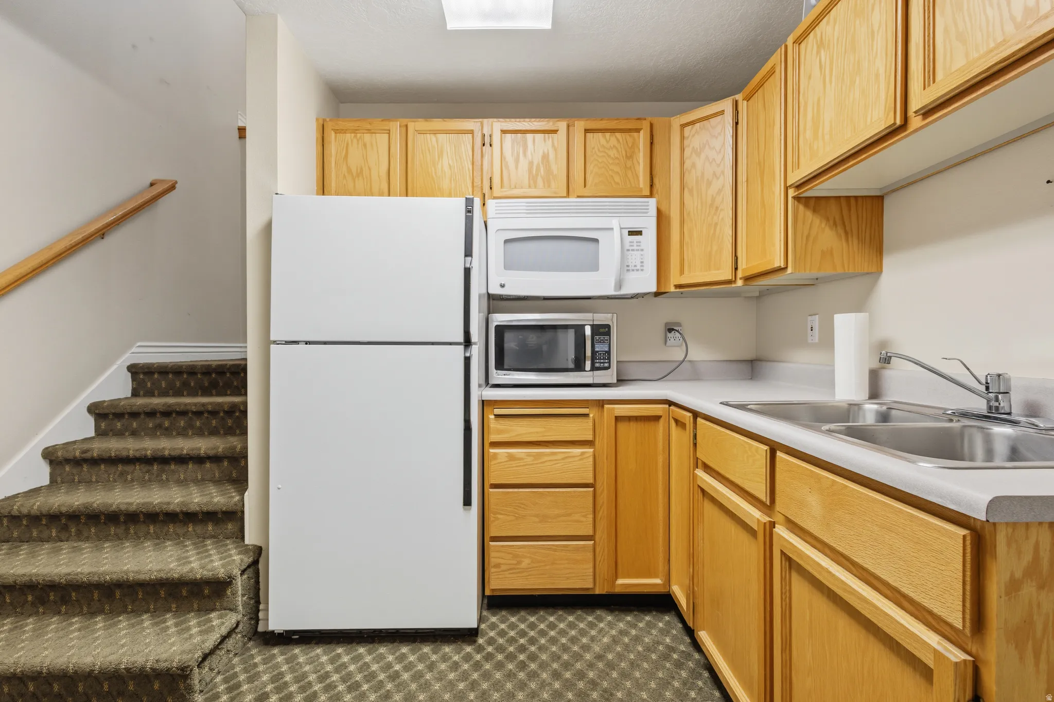 Kitchenette featuring light wood-finish cabinetry, a double basin stainless steel sink, and light-toned countertops