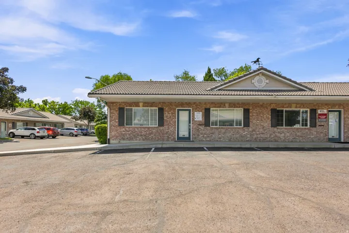 Brick-clad exterior featuring multiple entry points, a tile roof, decorative gable, and an expansive paved parking area