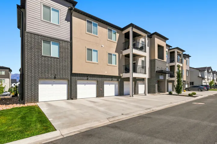 Multi-story residential complex featuring neutral-toned siding, dark brick facade, and integrated garage doors