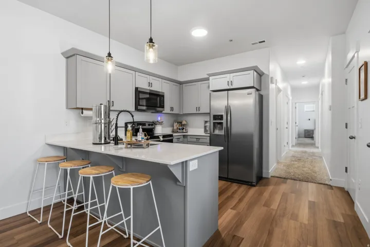 Open-concept kitchen featuring wood-finish flooring, light gray cabinetry, stainless steel appliances, and a central island with countertop seating