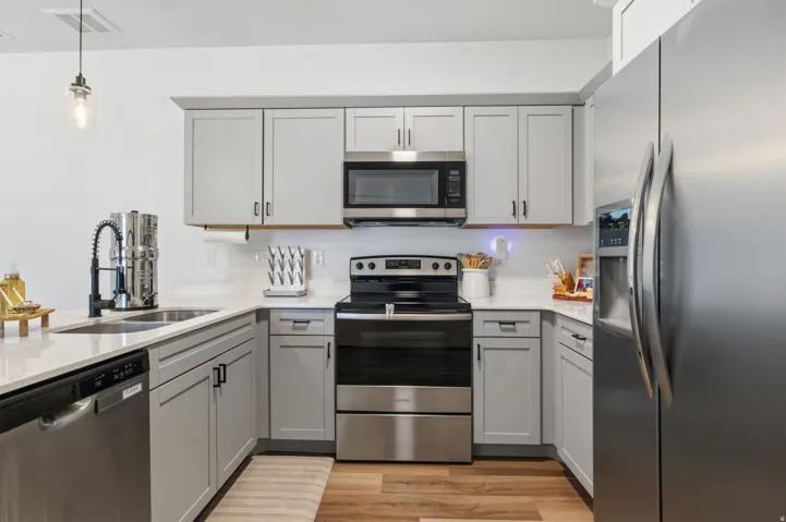 Kitchen featuring light gray cabinetry, stainless steel appliances, white countertops, and wood-finish flooring