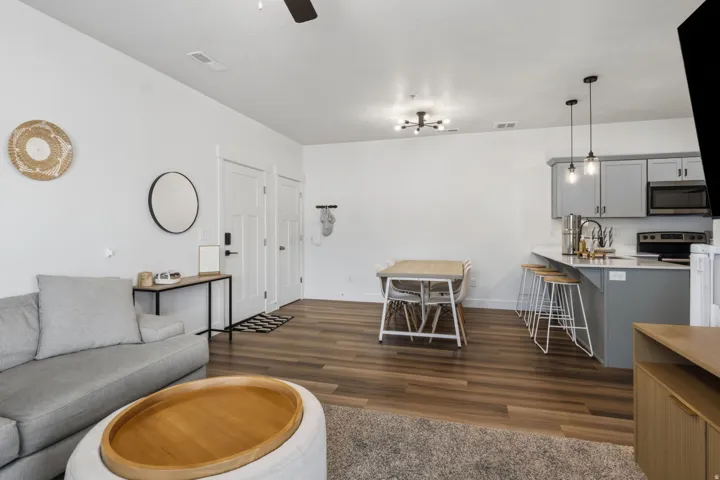 Open-concept living area featuring wood-finish flooring, a contemporary kitchen with grey cabinetry and an island, stainless steel appliances, and modern lighting fixtures