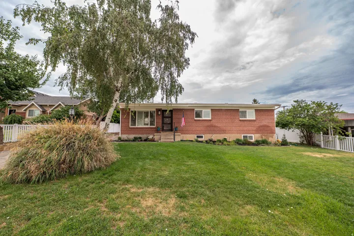 Brick-front residence featuring a mature birch tree, a manicured lawn, and white picket fencing