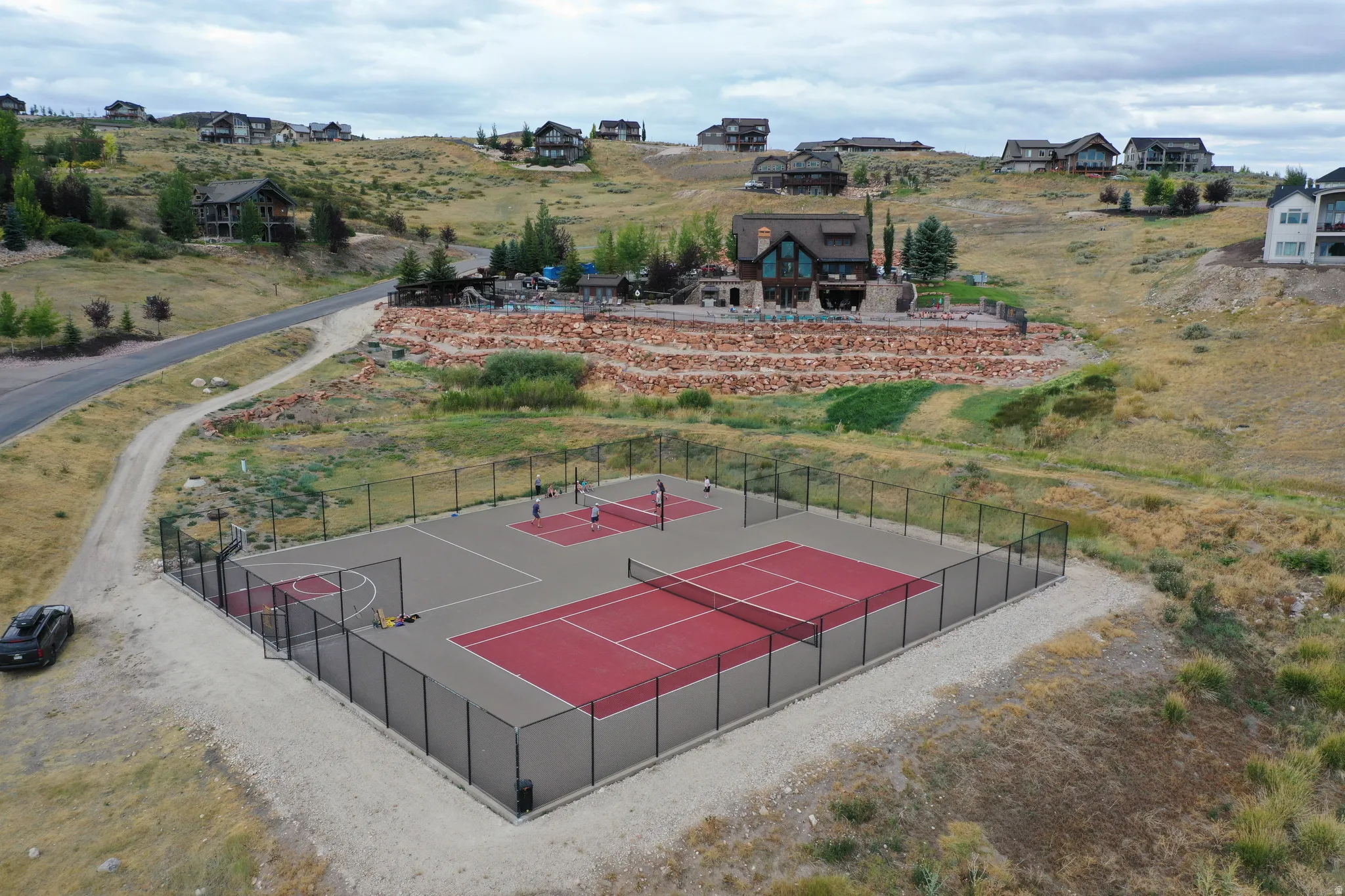 Multi-sport court featuring dedicated tennis and pickleball areas, a basketball hoop, and perimeter fencing