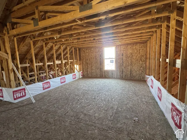 Unfinished space featuring exposed timber framing, oriented strand board flooring, and a singular window