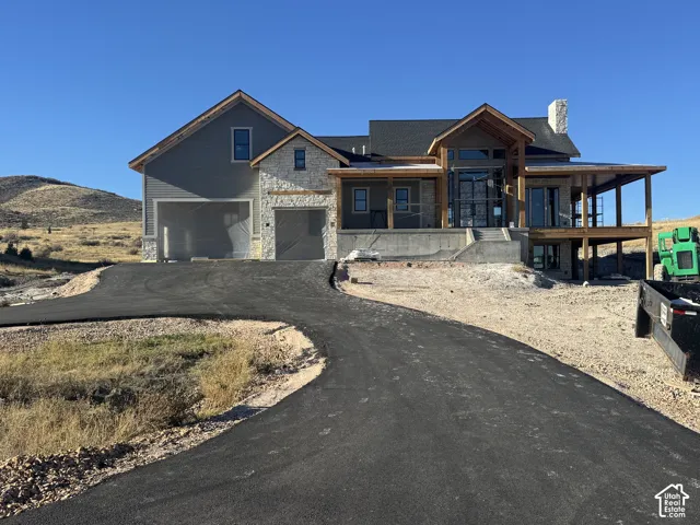 Exterior featuring stone and horizontal siding, asphalt driveway, covered porch with wood timber framing, and a multi-gabled roofline