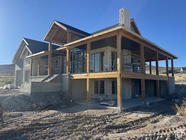 Custom stone exterior featuring heavy timber framing, expansive covered upper deck, lower-level patio, and tall stone chimney