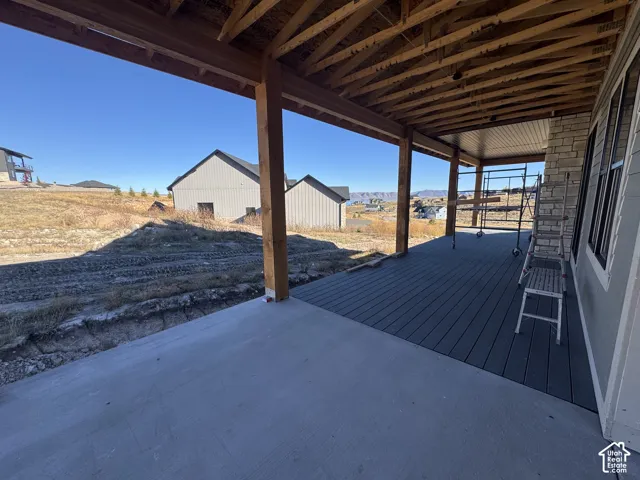 Covered patio featuring composite decking, exposed timber support beams, and stone exterior siding