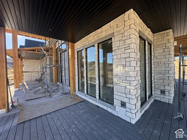 Covered outdoor space featuring composite decking, timber post framing, stone-veneer exterior cladding, and large-format windows with dark frames