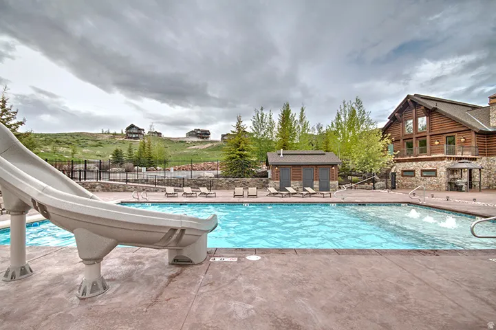 Outdoor pool area featuring a water slide, surrounding concrete patio, and a rustic log cabin-style building with stone accents