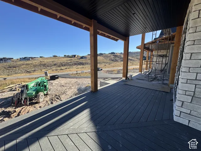 Covered patio featuring composite decking, exposed timber support beams, and a dark tongue-and-groove ceiling, complemented by exterior natural stone cladding