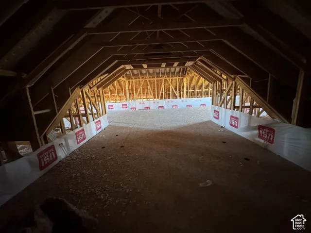 Unfinished attic space featuring exposed wood timber framing, engineered wood flooring, and perimeter building wrap