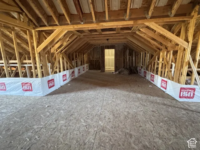 Unfinished attic space featuring exposed wood truss framing, oriented strand board flooring, and installed vapor barrier sheathing
