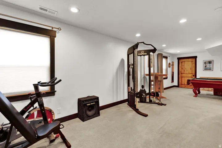 Spacious finished basement featuring recessed lighting, a window with wood trim, and a rustic wood door