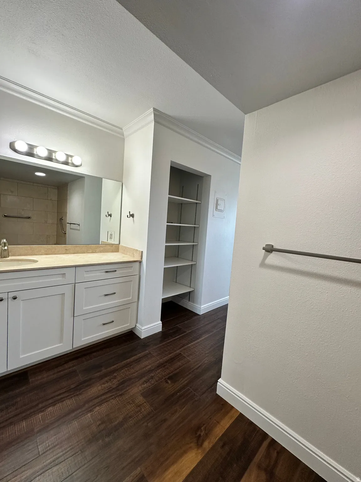 Bathroom featuring a dual-sink vanity with light-toned countertops, white cabinetry, and dark wood-finish flooring