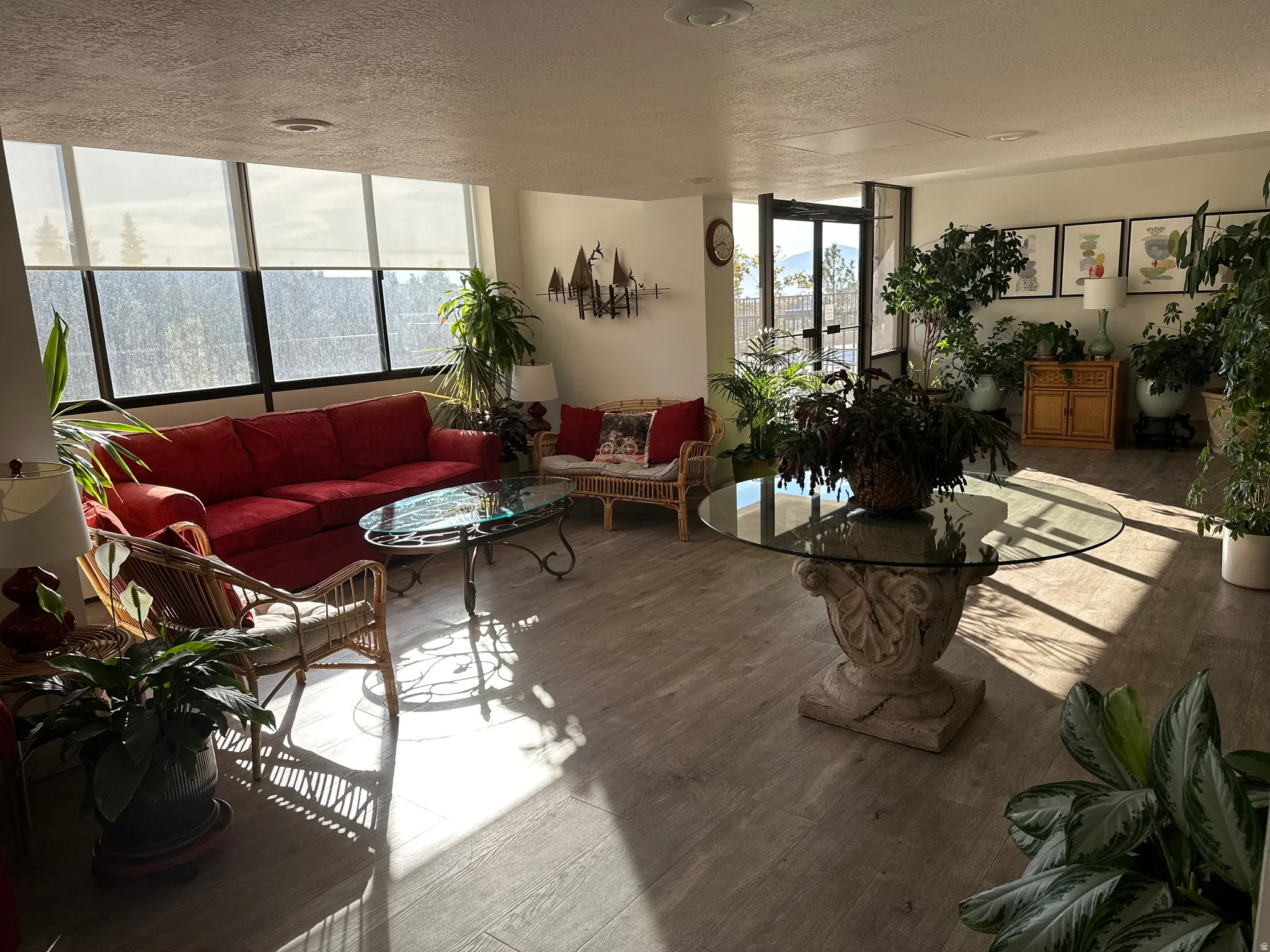 Spacious common area featuring extensive window treatments, light wood-finish flooring, and a glass-top table with a decorative stone base