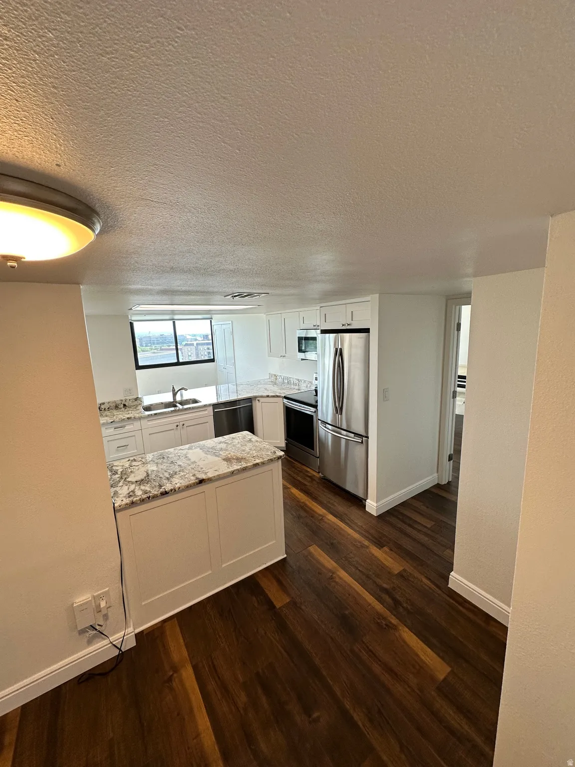 Modern kitchen featuring white cabinetry, granite countertops, stainless steel appliances, wood-finish flooring, and an integrated breakfast bar