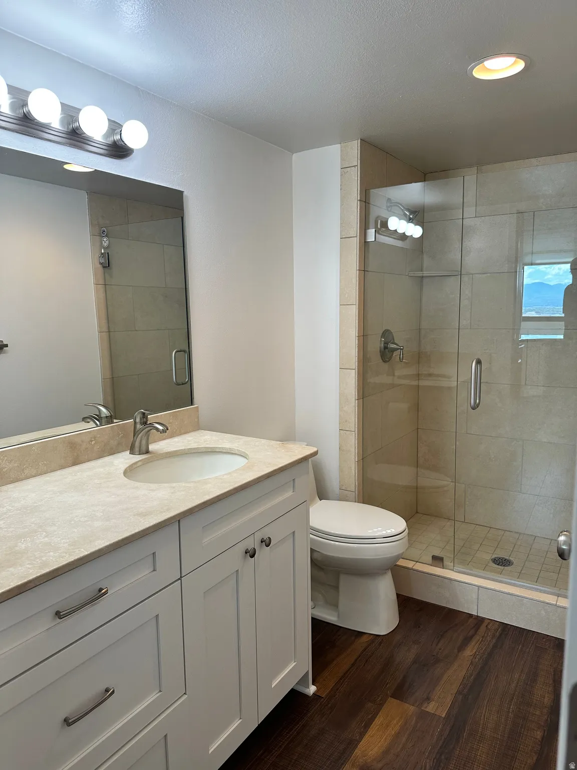 Bathroom featuring a white vanity with an integrated sink, a light-toned countertop, and wood-finish flooring