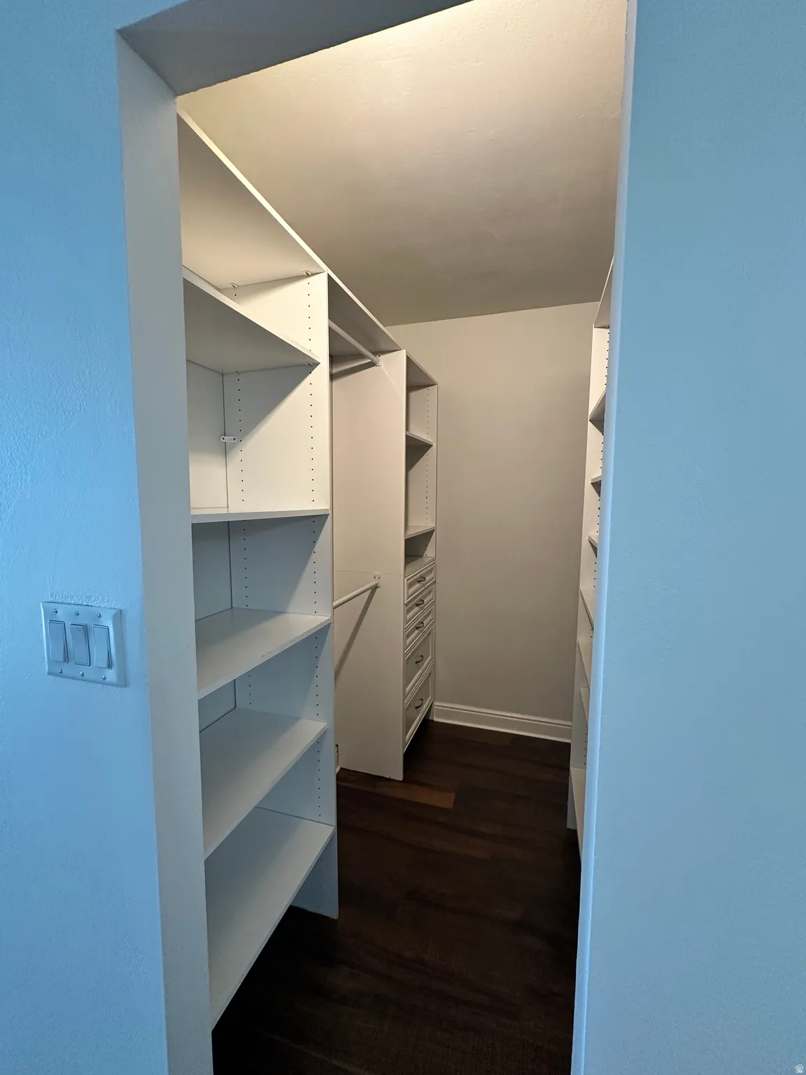 Custom walk-in closet featuring white shelving units, built-in drawers, and dark wood-finish flooring