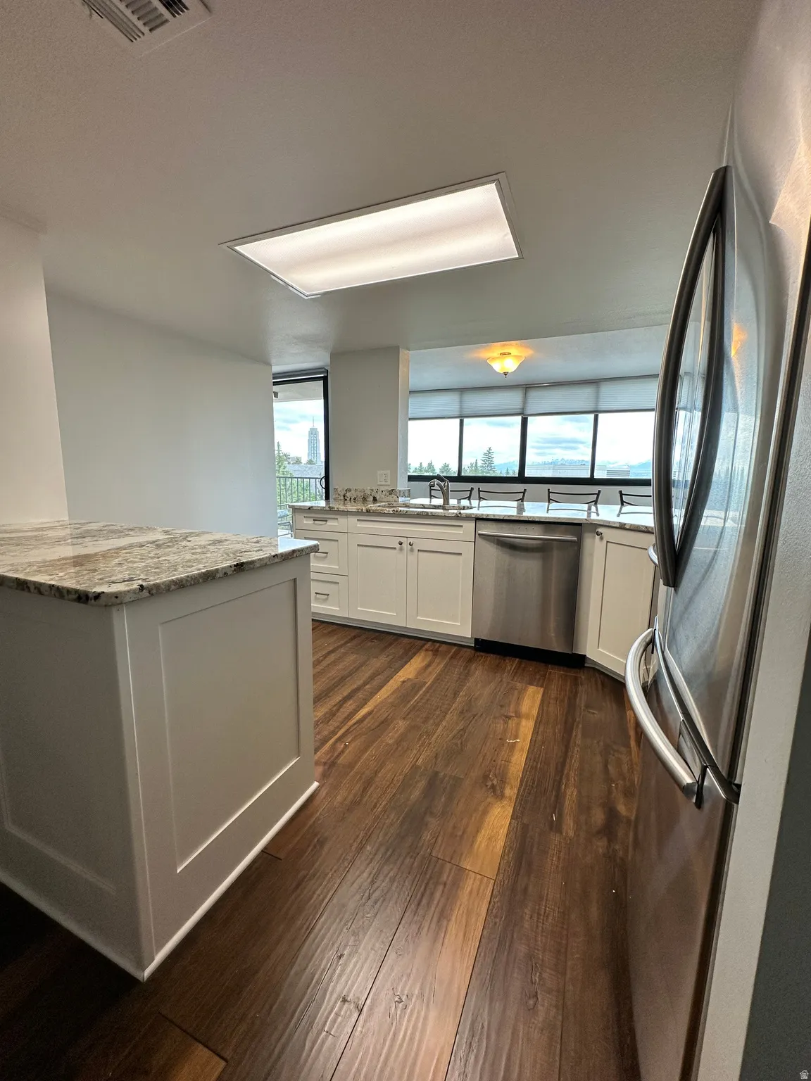 Kitchen featuring wood-finish flooring, white cabinetry, granite countertops, and stainless steel appliances