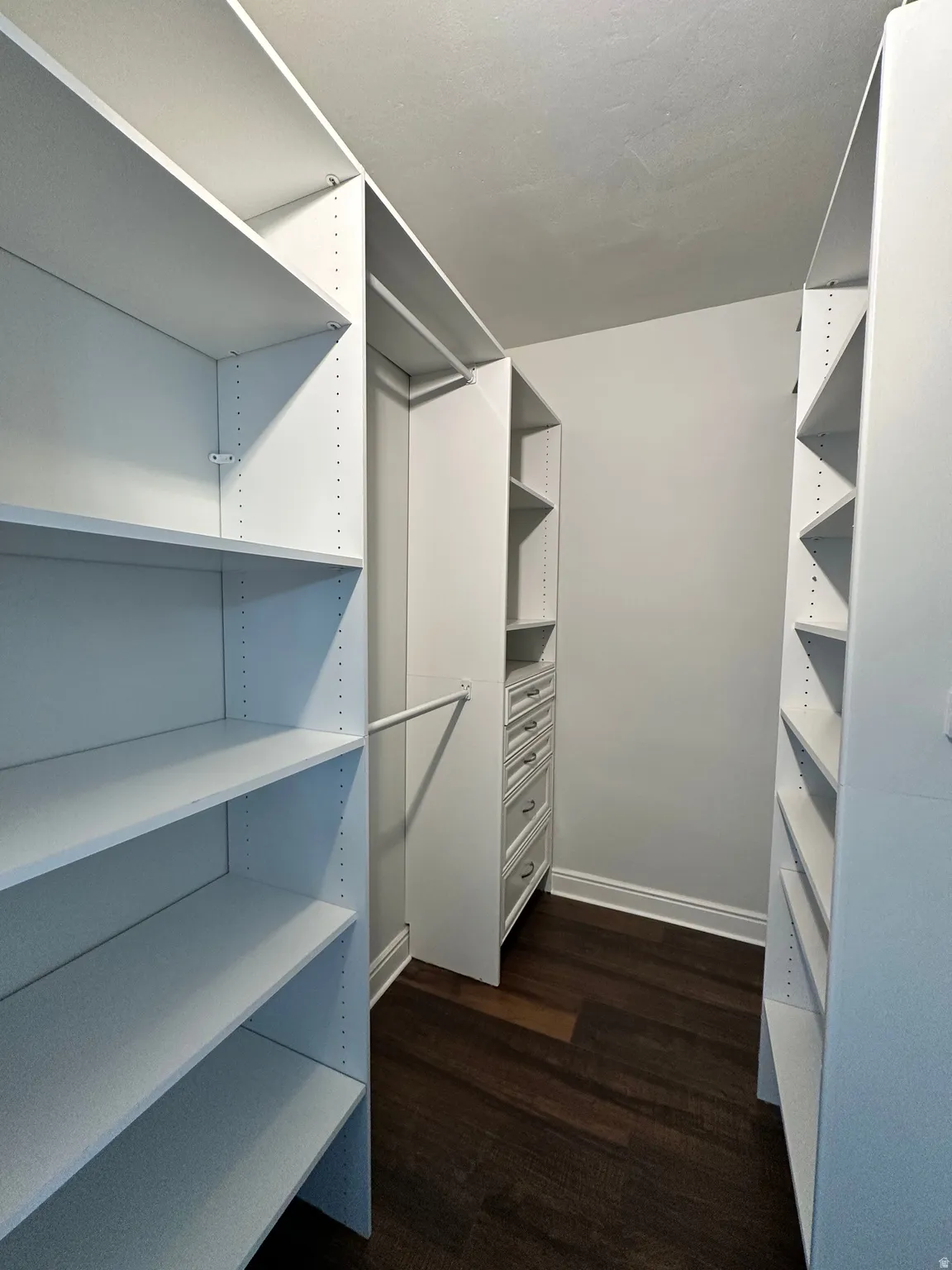 Built-in closet system featuring white shelving, multiple hanging rods, integrated drawers with brushed nickel hardware, and wood-finish flooring