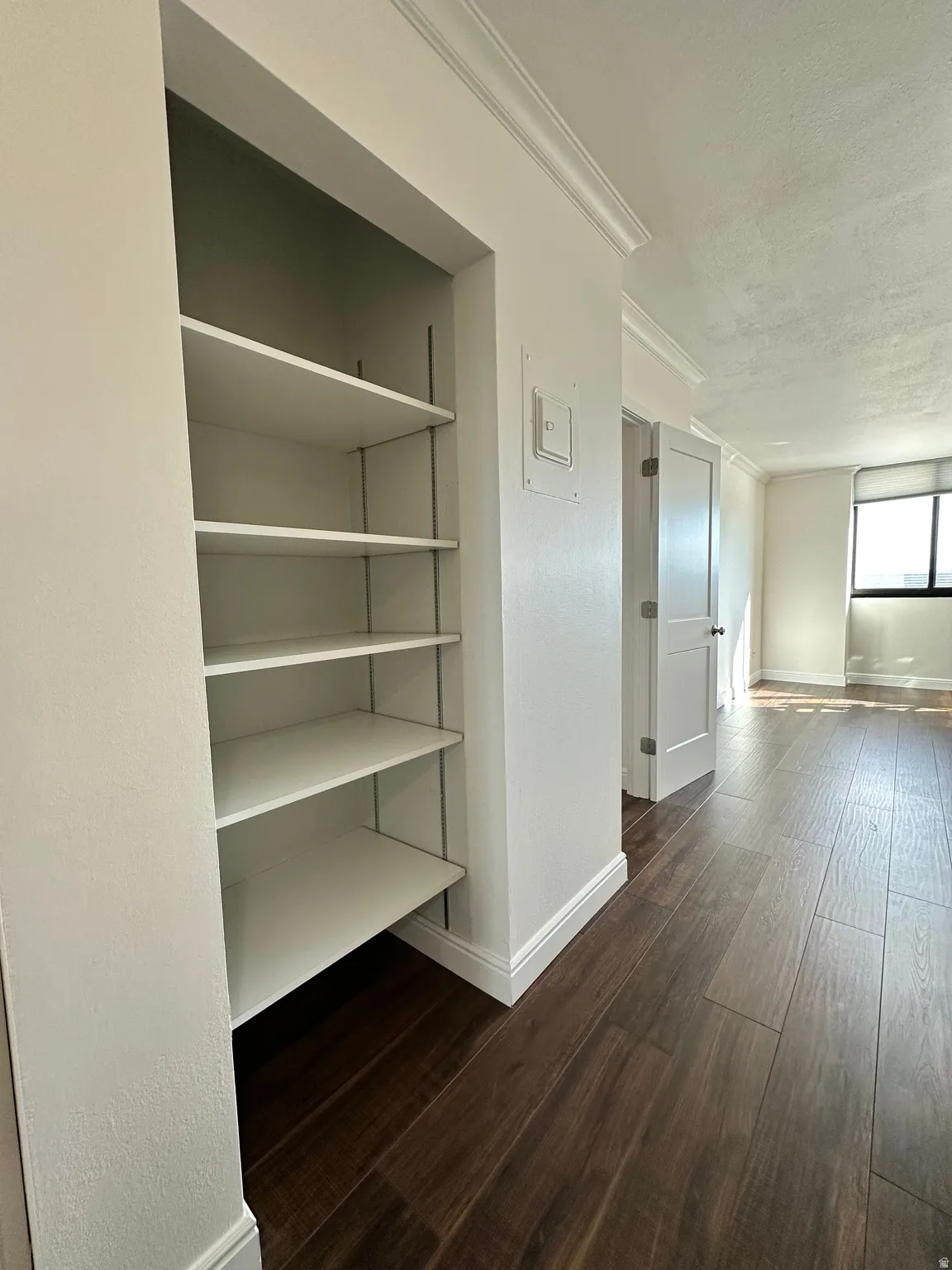 Built-in shelving unit with adjustable white shelves, dark wood-finish flooring, white baseboards, and crown molding
