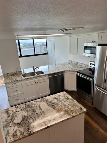 Contemporary kitchen featuring an island, white cabinetry, granite countertops, stainless steel appliances, and wood-finish flooring