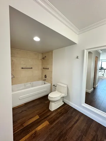 Bathroom featuring a full tub with stone tile surround, wood-finish flooring, white toilet, and recessed lighting