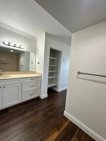 Bathroom featuring a dual-sink vanity with light-toned countertops, white cabinetry, and dark wood-finish flooring