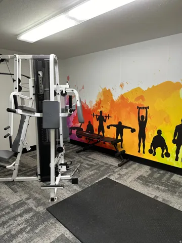 Dedicated fitness space featuring a multi-station exercise machine, free weight bench, and a large rubber mat