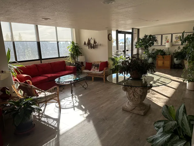 Spacious common area featuring extensive window treatments, light wood-finish flooring, and a glass-top table with a decorative stone base