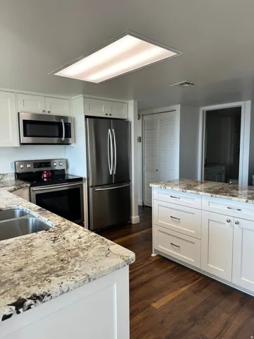 Kitchen featuring white shaker cabinetry, stainless steel appliances, speckled countertops, and wood-finish flooring