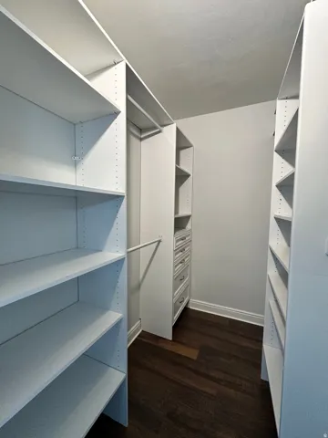 Built-in closet system featuring white shelving, multiple hanging rods, integrated drawers with brushed nickel hardware, and wood-finish flooring