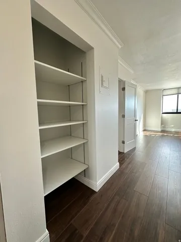 Built-in shelving unit with adjustable white shelves, dark wood-finish flooring, white baseboards, and crown molding