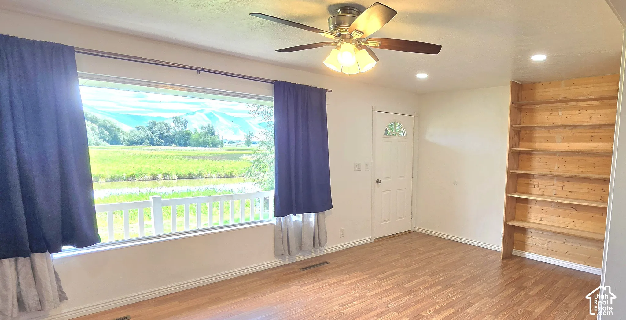 Expansive window with a white railing, wood-finish flooring, built-in wooden shelving, a ceiling fan with integrated lighting, and recessed lighting