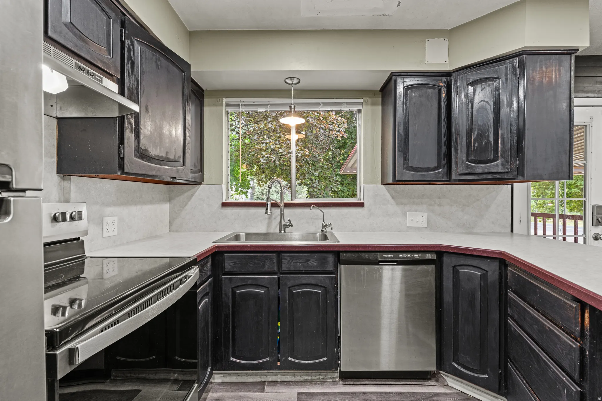 Kitchen featuring cabinetry, light countertops, stainless steel appliances, a window over the sink, and wood-finish flooring