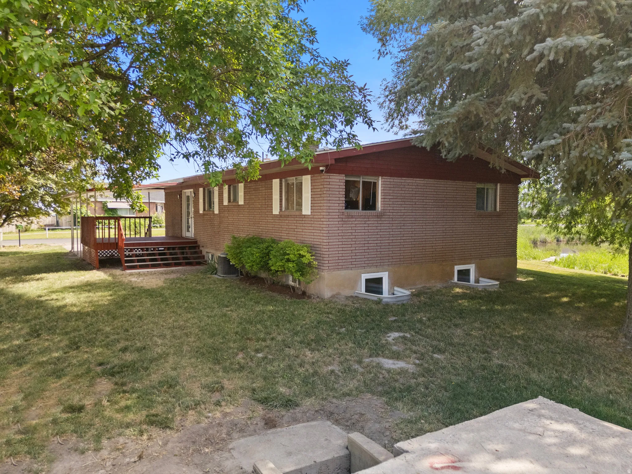Brick exterior featuring a wood deck with lattice railing, multiple windows, and mature trees providing shade