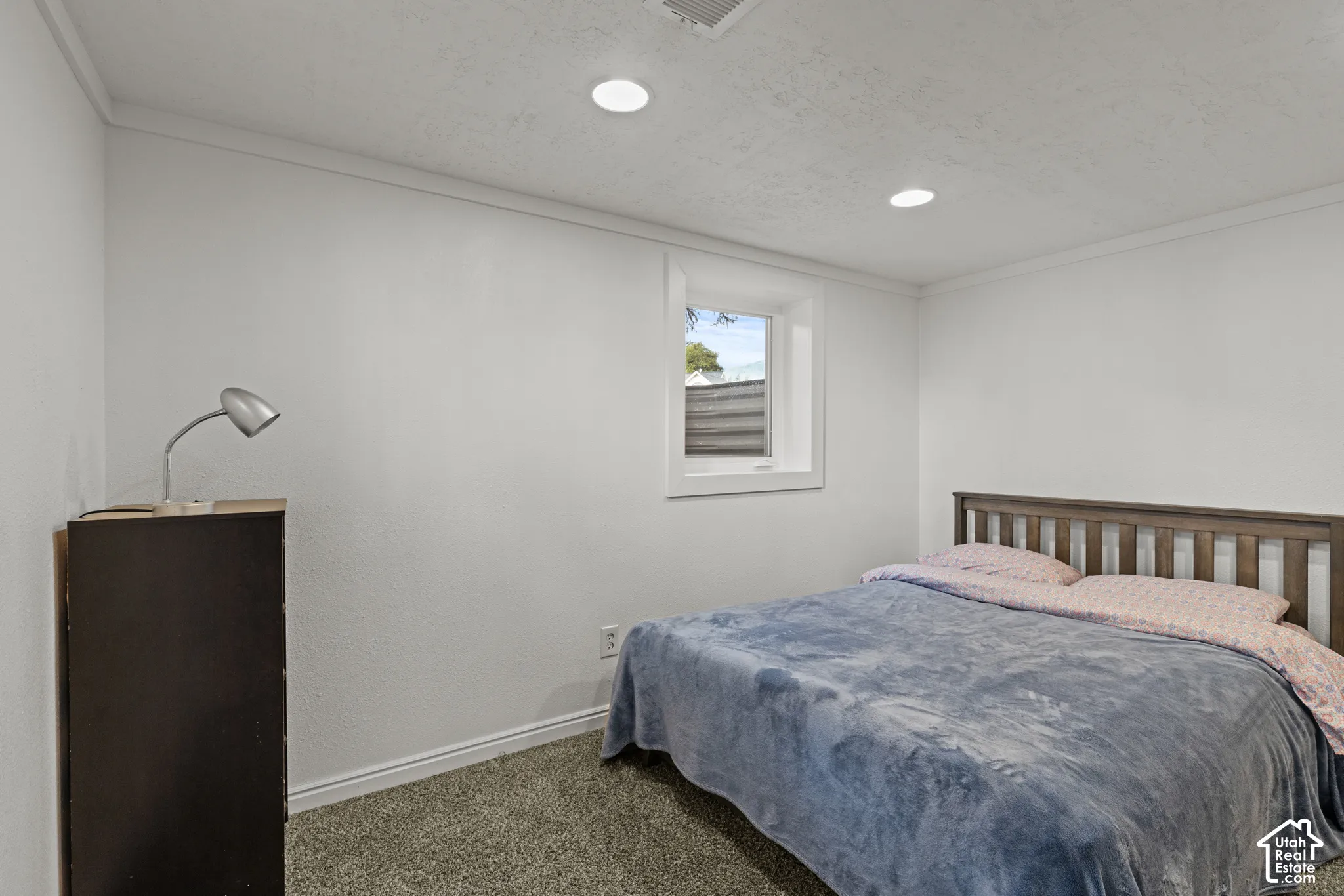 Recessed lighting illuminates a room featuring a window with white trim, and white walls.