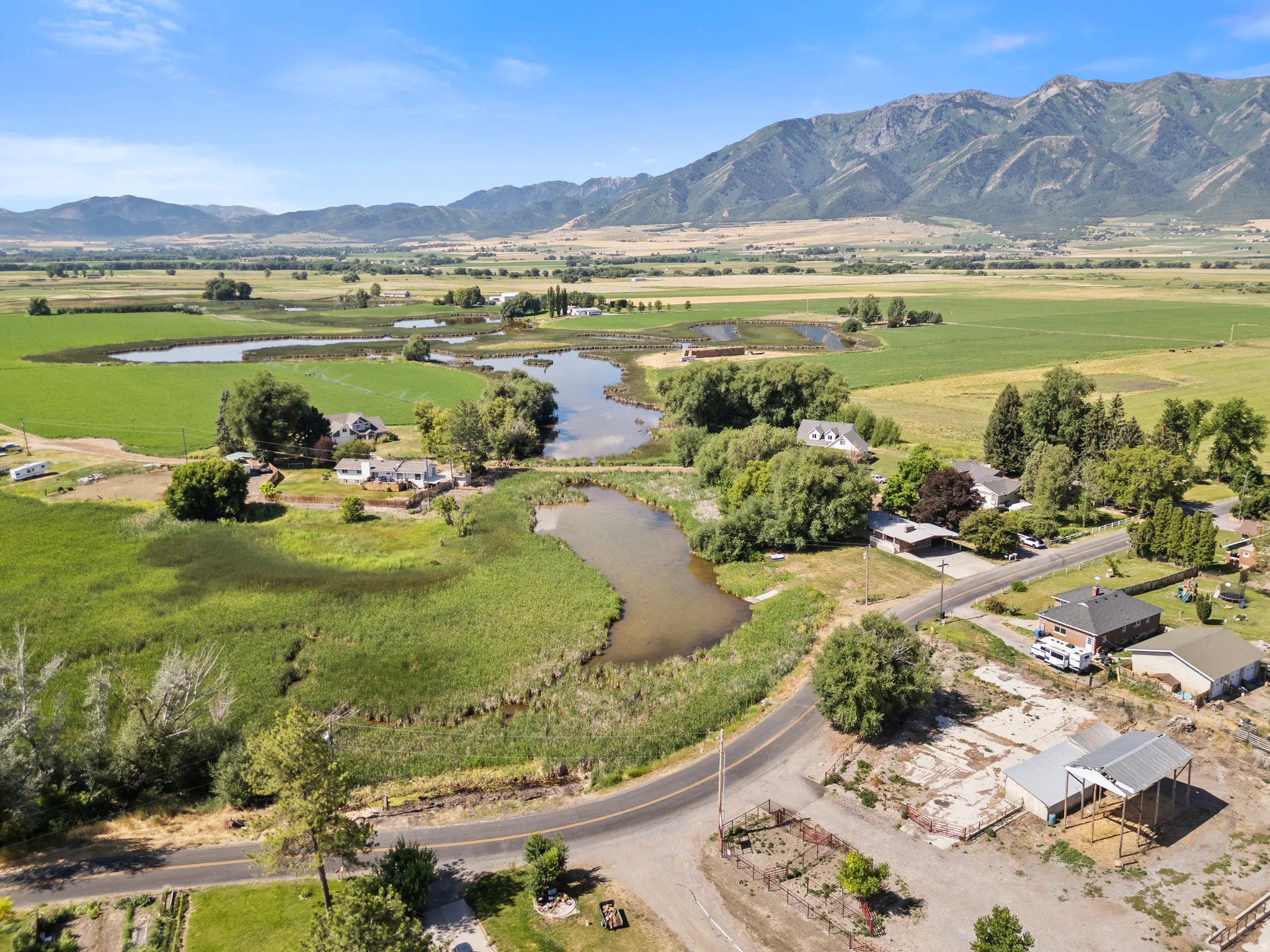 Expansive rural landscape featuring a road, pond, and distant mountains