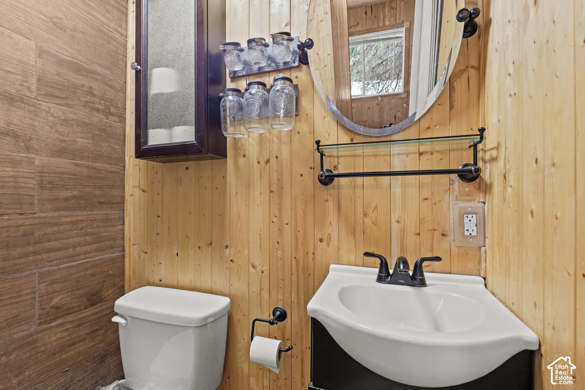 Corner pedestal sink with black hardware, flanked by natural wood plank walls